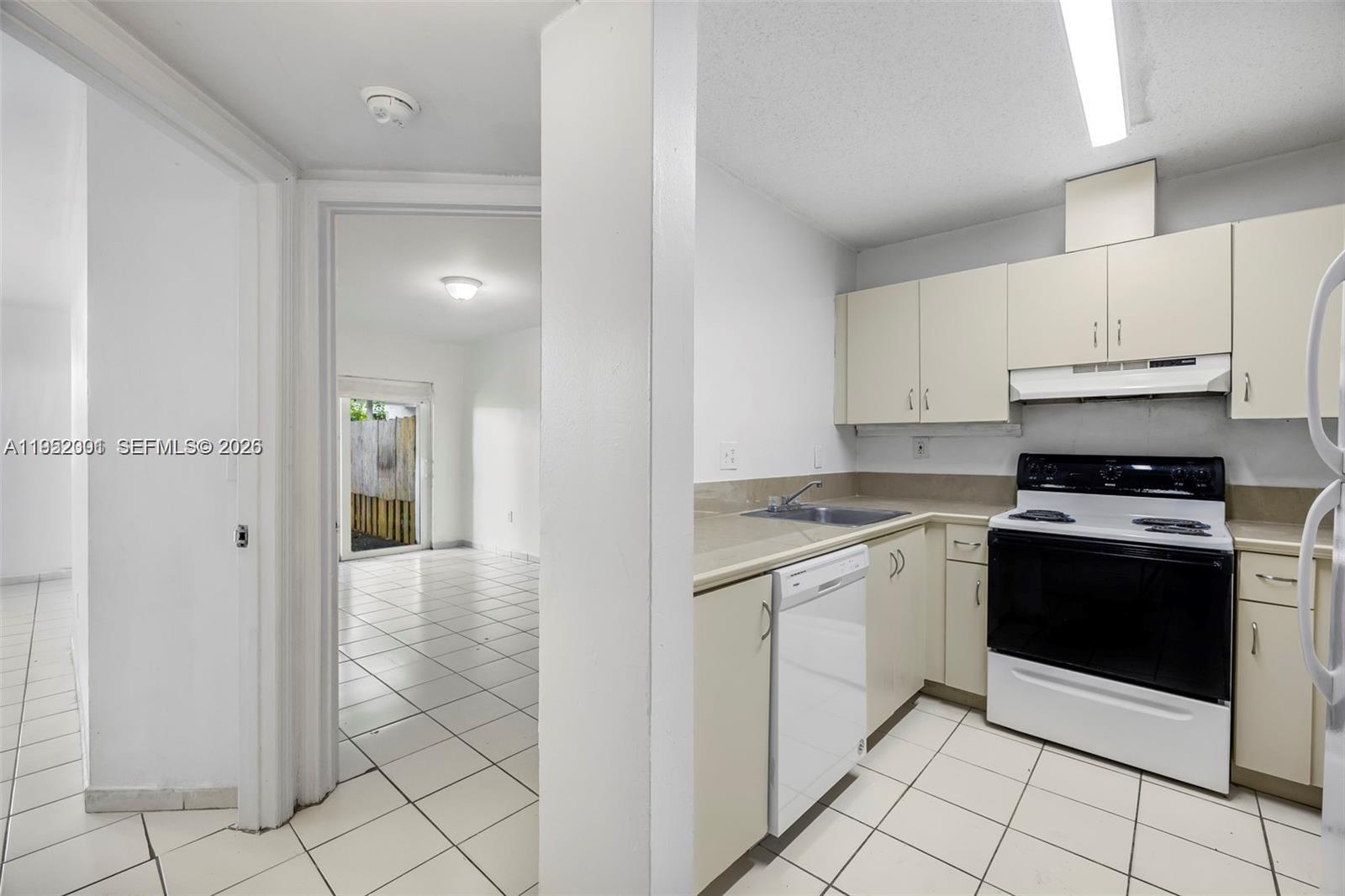 A kitchen with white cabinets and appliances opens to a tiled room with a patio door — 8421 SW 209th St # 8421, Cutler Bay FL 33189, CUTLER BAY, FL
