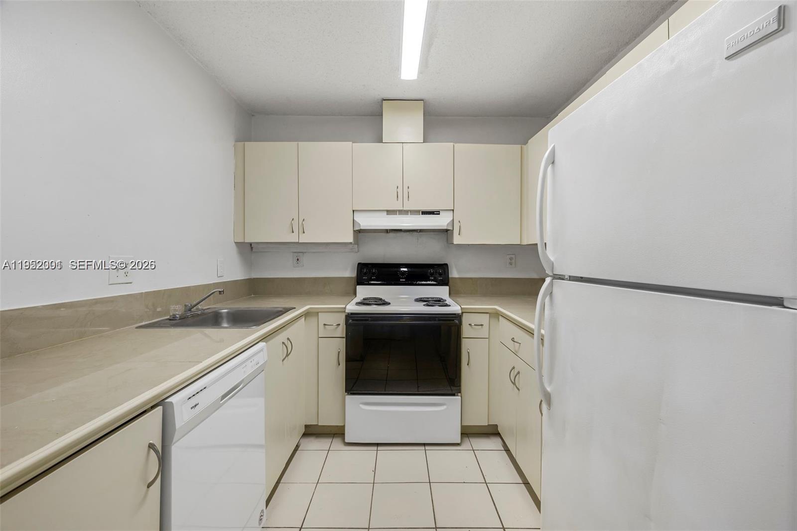A galley-style kitchen features white appliances, beige cabinets, and light-colored tile flooring — 8421 SW 209th St # 8421, Cutler Bay FL 33189, CUTLER BAY, FL