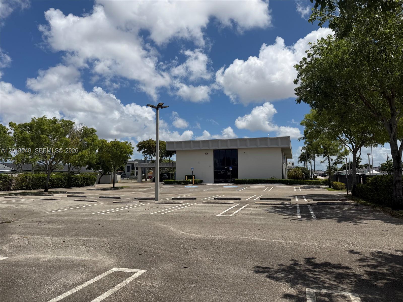 A single-story commercial building sits behind a large, empty asphalt parking lot under a cloudy sky — 1601 E 4th Ave, Hialeah FL 33010, HIALEAH, FL