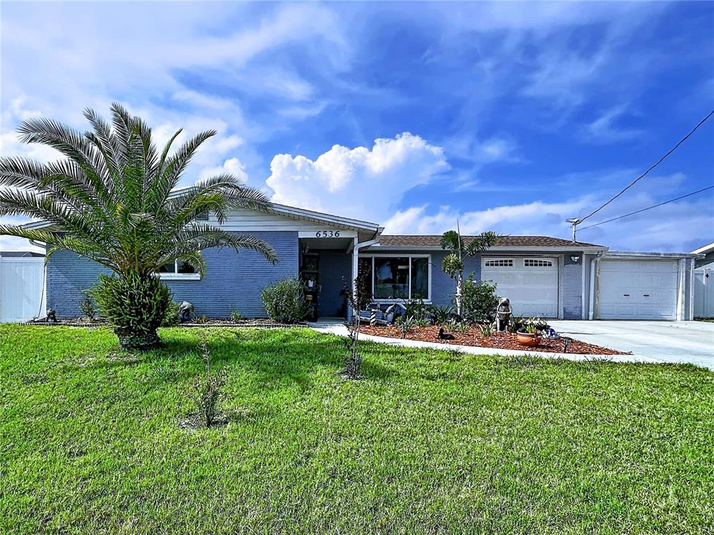 A single-story blue brick house features a palm tree, a front lawn, and two garages — 6536 LEESIDE ISLE, HUDSON, FL