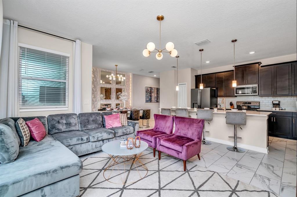 An open-concept living room and kitchen featuring a grey sectional, purple chairs, and dark cabinetry — 640 PEBBLE BEACH DRIVE, DAVENPORT, FL
