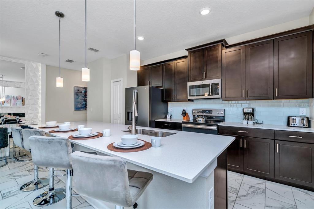 A modern kitchen features dark wood cabinets, white countertops, a large island, and pendant lighting — 640 PEBBLE BEACH DRIVE, DAVENPORT, FL
