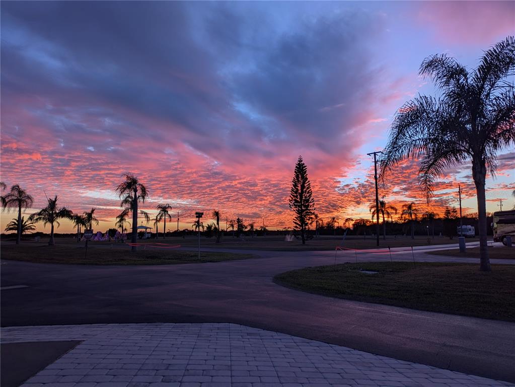 A vibrant sunset illuminates the sky over a paved road lined with palm trees — 46900 BERMONT ROAD UNIT 1L, PUNTA GORDA, FL