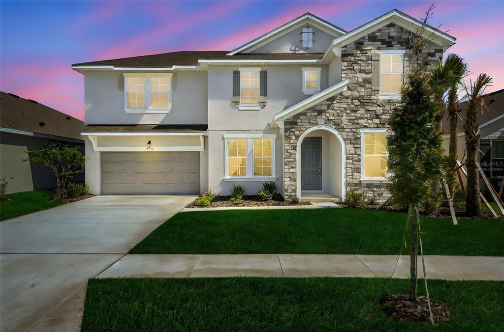 A two-story suburban house with a stone facade, gray garage, and a green lawn — 17453 VALLEYWOOD PARKWAY, LAND O LAKES, FL