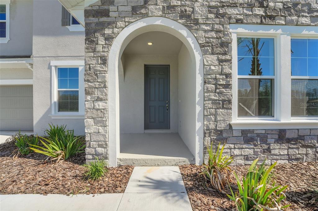 A stone-faced entryway features an arched porch leading to a dark gray front door — 17453 VALLEYWOOD PARKWAY, LAND O LAKES, FL