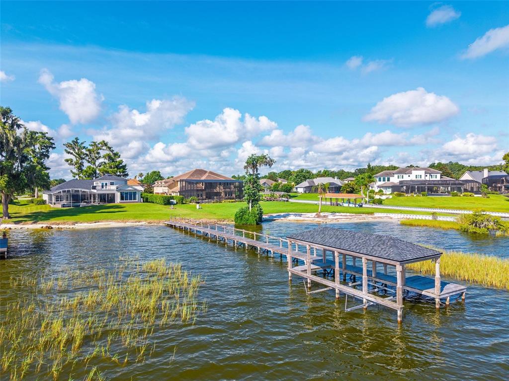 An aerial view shows a long wooden dock extending into a lake toward several houses — 7303 BIRDS NEST COURT, YALAHA, FL