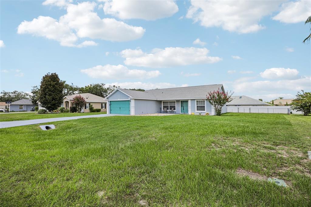 A light blue single-story house with a teal garage door sits on a grassy lot — 5705 SW 89TH PLACE, OCALA, FL
