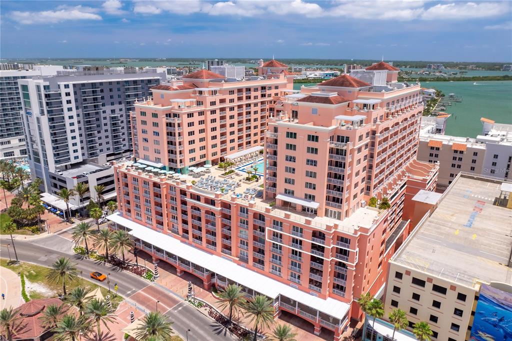 An aerial view of a large, peach-colored multi-story resort building near the water — 301 S GULFVIEW BOULEVARD UNIT 604, CLEARWATER BEACH, FL