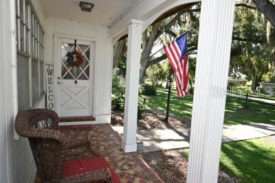 A covered front porch features a wicker chair, a white door, and an American flag — 35833 LAKESHORE DRIVE, DADE CITY, FL