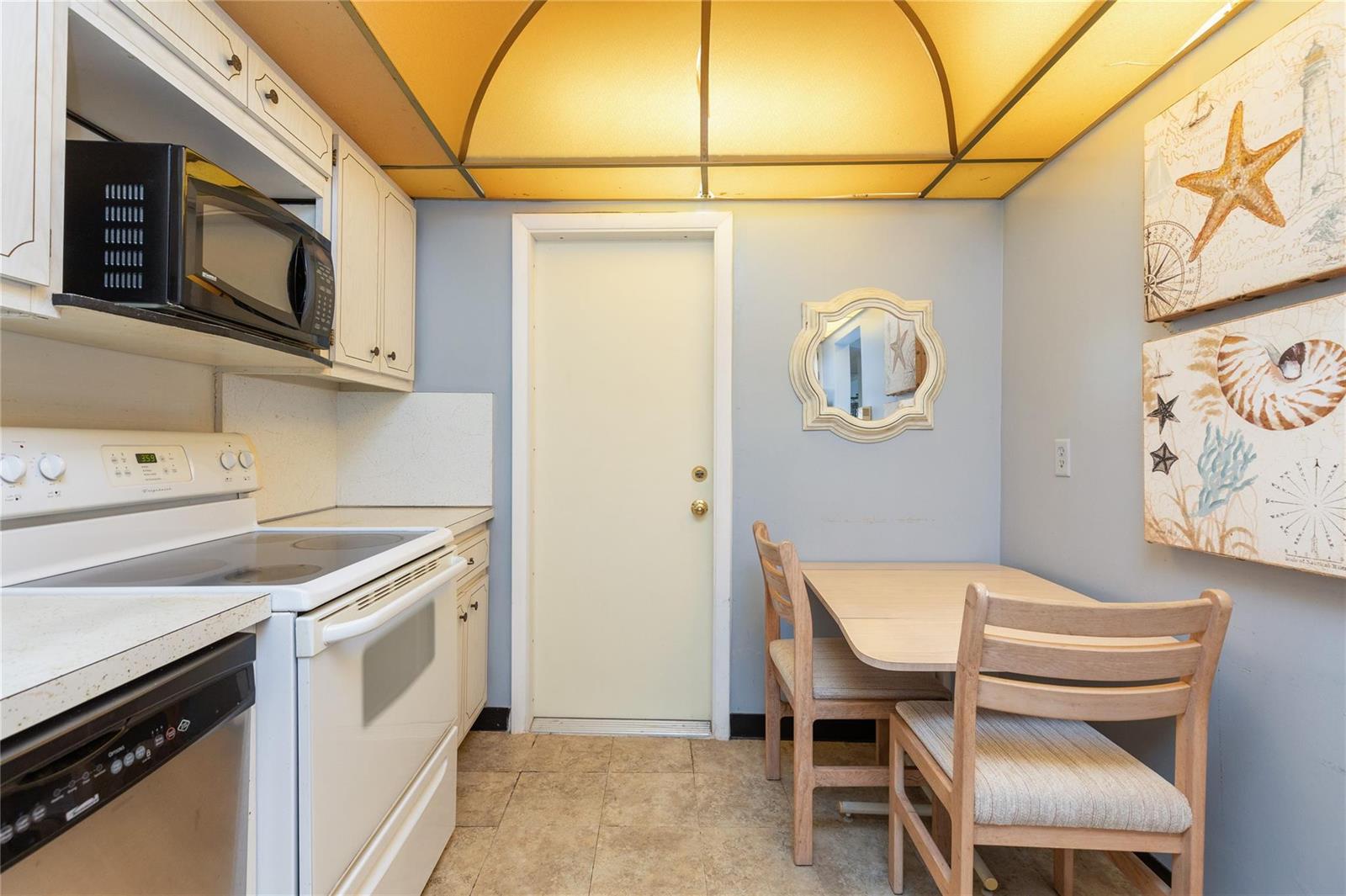 A kitchen features white appliances, light wood cabinets, a small dining table, and yellow lighting — 2731 NE 14th St Causeway # 121, Pompano Beach FL 33062, POMPANO BEACH, FL