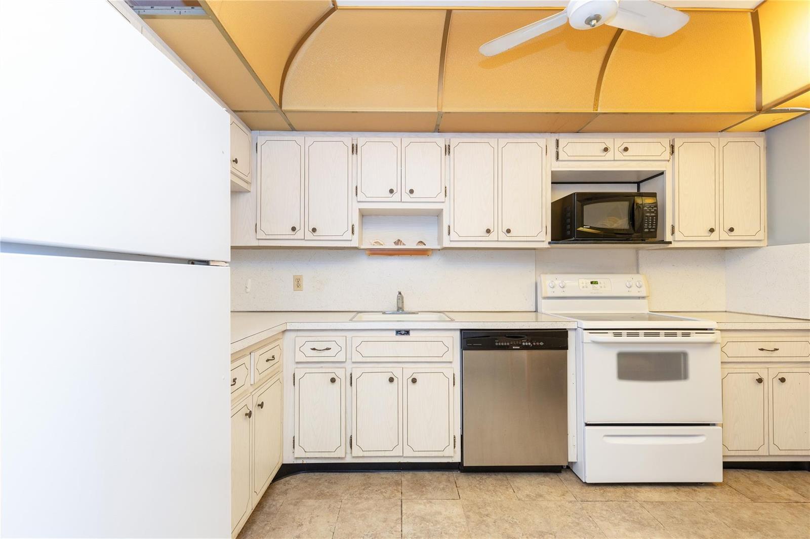 A kitchen features white cabinets, a stainless steel dishwasher, a white stove, and yellow ceiling — 2731 NE 14th St Causeway # 121, Pompano Beach FL 33062, POMPANO BEACH, FL