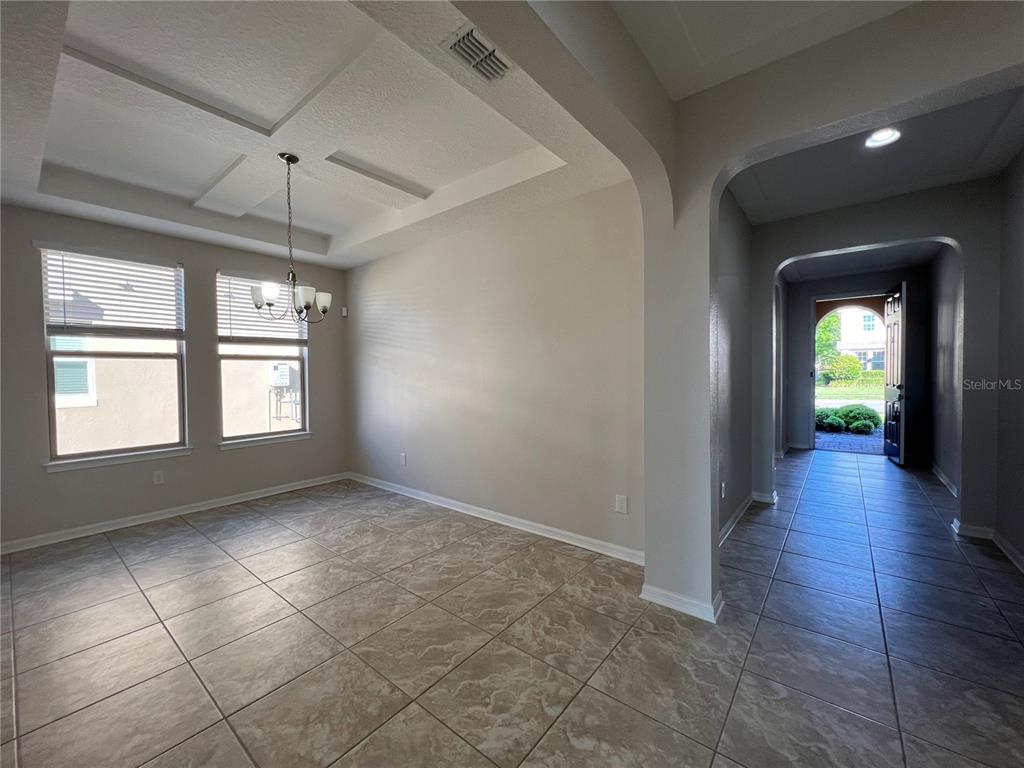 A dining room with a coffered ceiling and tile flooring leads to an arched entryway — 17392 BAL HARBOUR DRIVE, WINTER GARDEN, FL