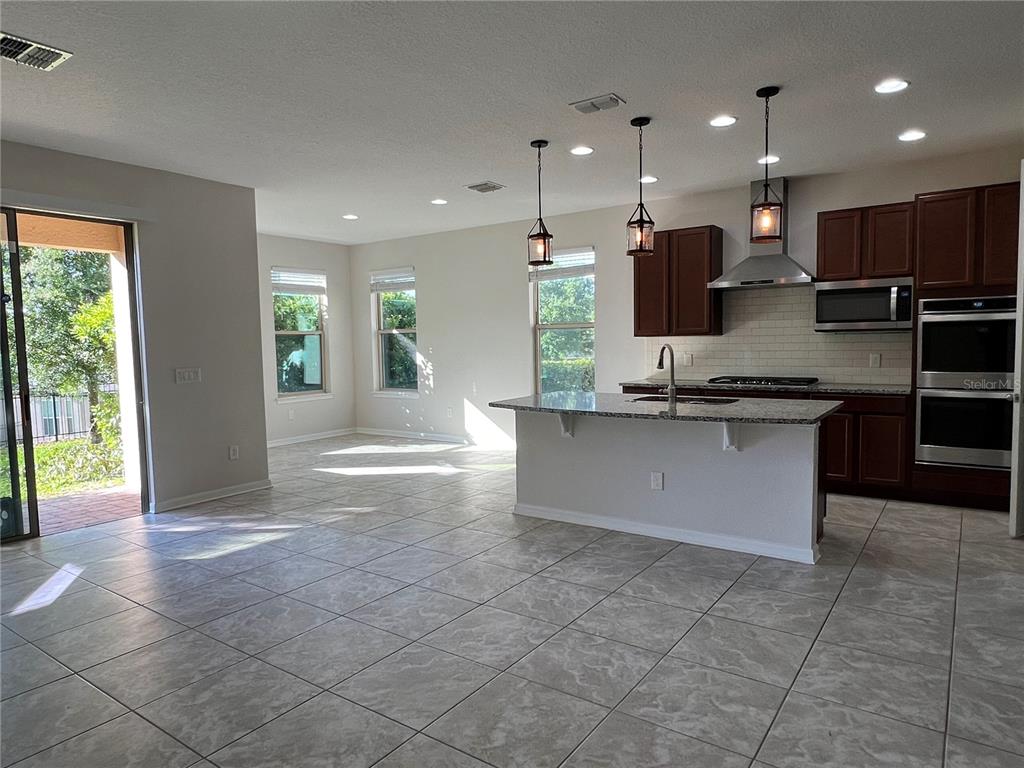 A kitchen with dark wood cabinets, granite countertops, and tile flooring opens to a living area — 17392 BAL HARBOUR DRIVE, WINTER GARDEN, FL