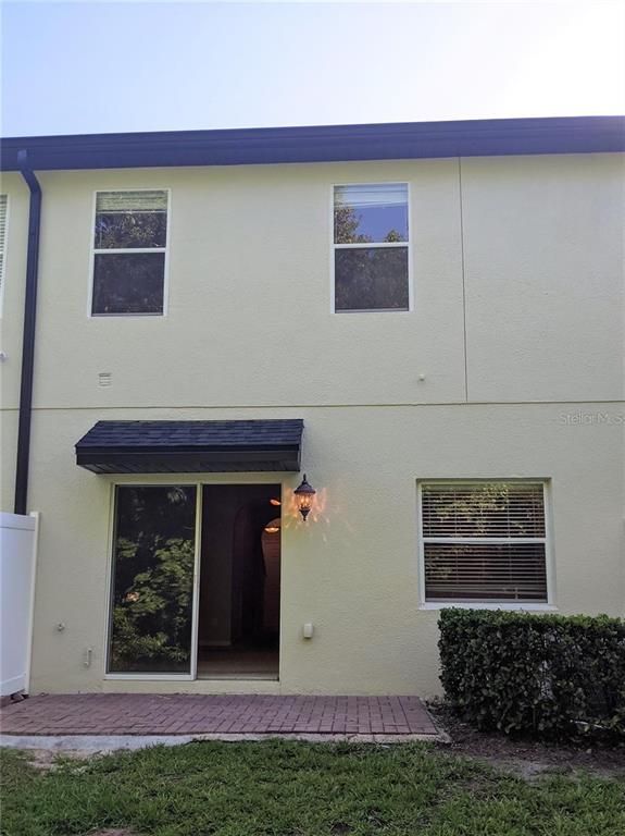 The exterior rear view of a two-story townhouse features a brick patio and sliding doors — 10272 PARK COMMONS DRIVE, ORLANDO, FL