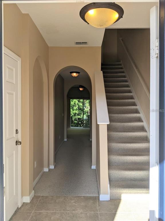 An entryway with a tiled floor, carpeted stairs, and arched transitions leading to a back room — 10272 PARK COMMONS DRIVE, ORLANDO, FL