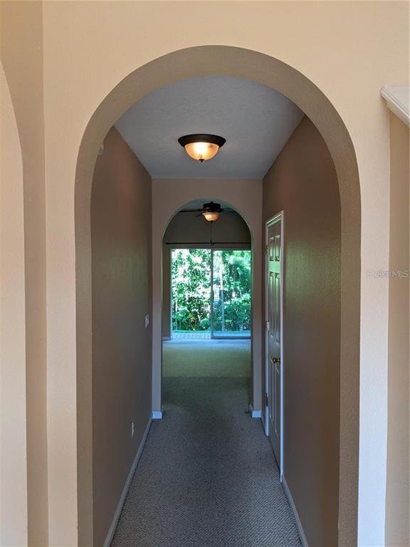 A hallway with arched entryways leads to a room with a sliding glass door — 10272 PARK COMMONS DRIVE, ORLANDO, FL