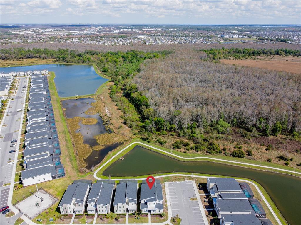 An aerial view shows a row of townhouses adjacent to a pond and wooded area — 2901 PROTAGONIST STREET, KISSIMMEE, FL
