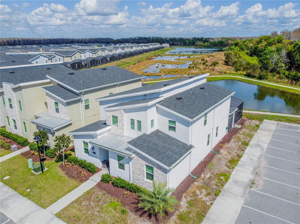 An aerial view shows a modern two-story townhouse with a stone facade near a pond — 2901 PROTAGONIST STREET, KISSIMMEE, FL