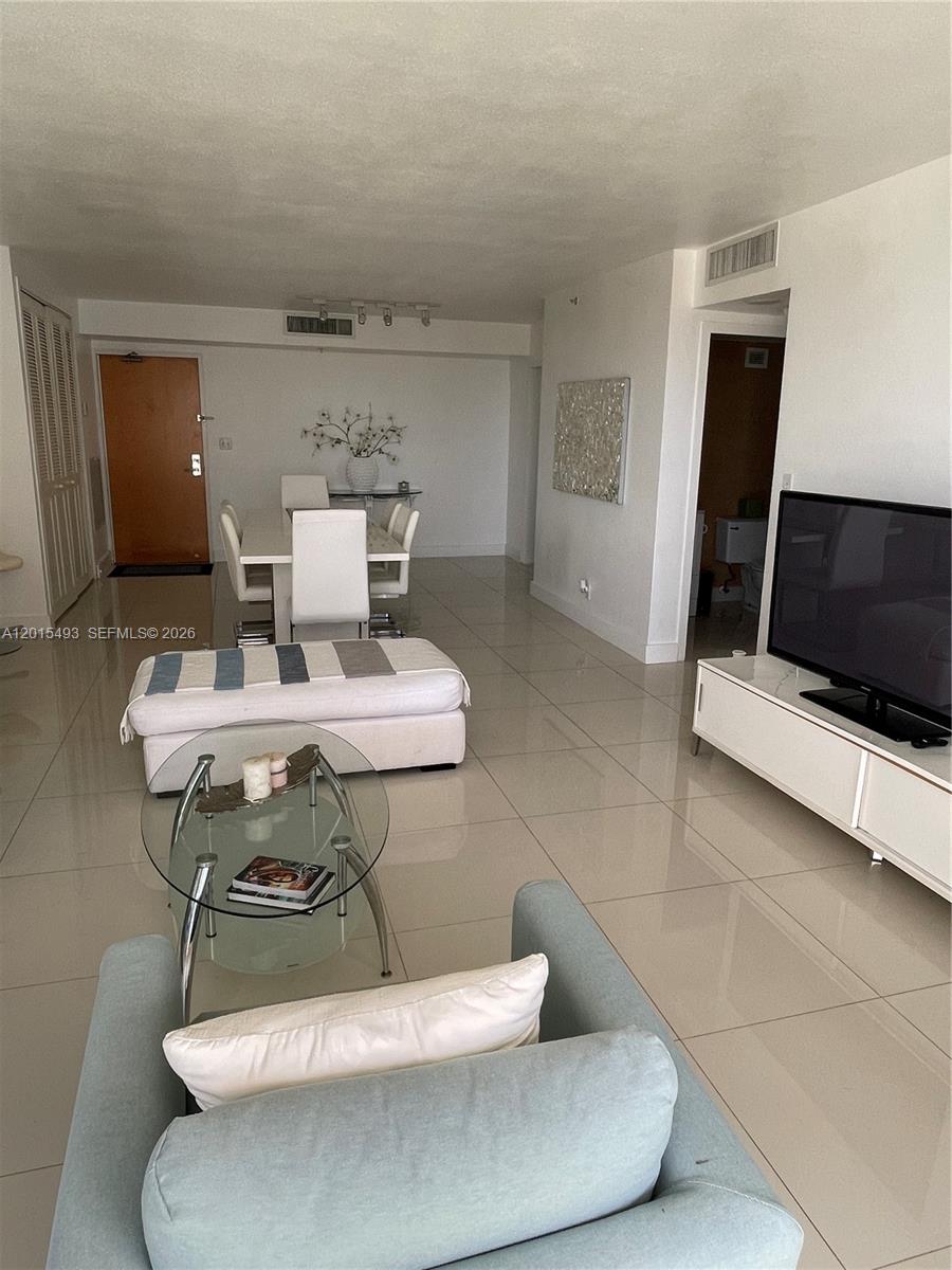 A bright living and dining area features white tile flooring, modern furniture, and a television — 9195 Collins Ave # 1012, Surfside FL 33154, SURFSIDE, FL