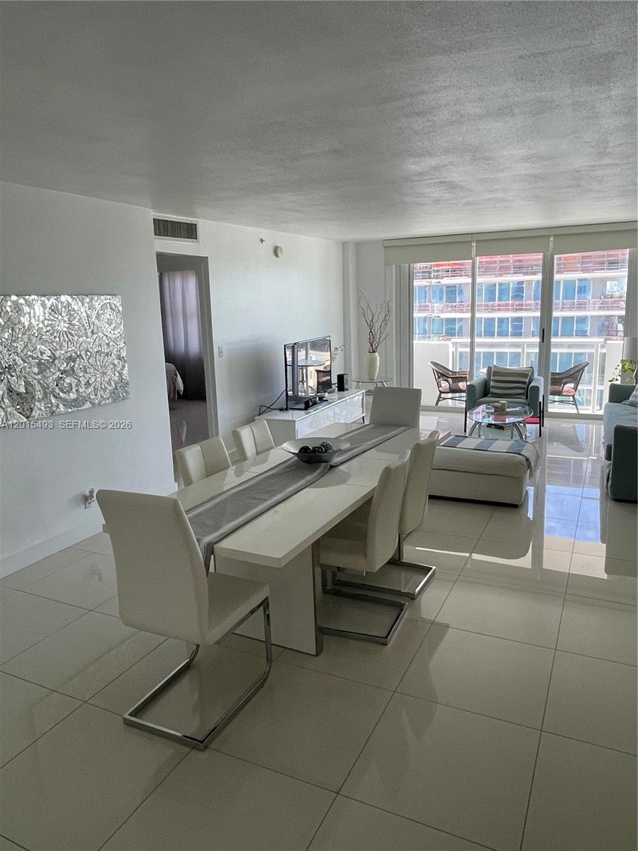 A kitchen features white cabinets, a glass dining table, and light-colored tile flooring — 9195 Collins Ave # 1012, Surfside FL 33154, SURFSIDE, FL