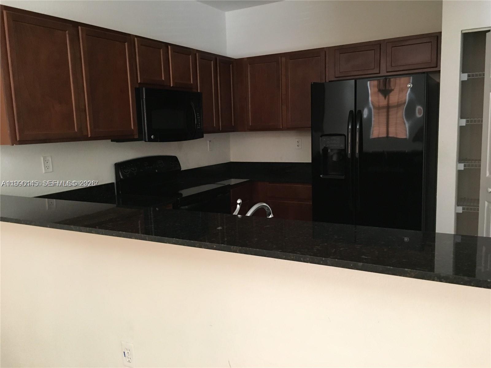A kitchen features dark wood cabinets, black appliances, and a black granite countertop breakfast bar — 10870 NW 88th Ter # 223, Doral FL 33178, DORAL, FL