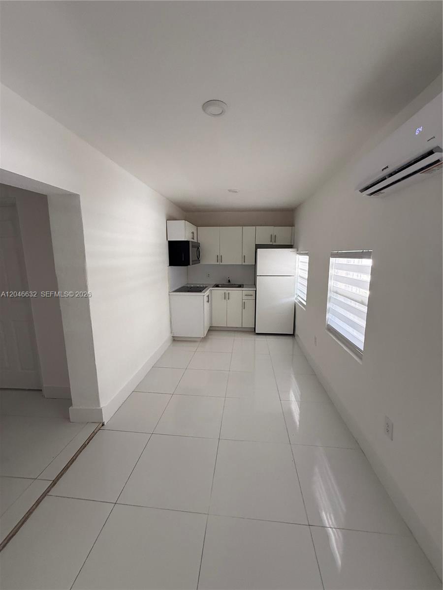 A small kitchen features white cabinets, tile flooring, and a wall-mounted air conditioning unit — 6716 NW 6th Ave # 2, Miami FL 33150, MIAMI, FL