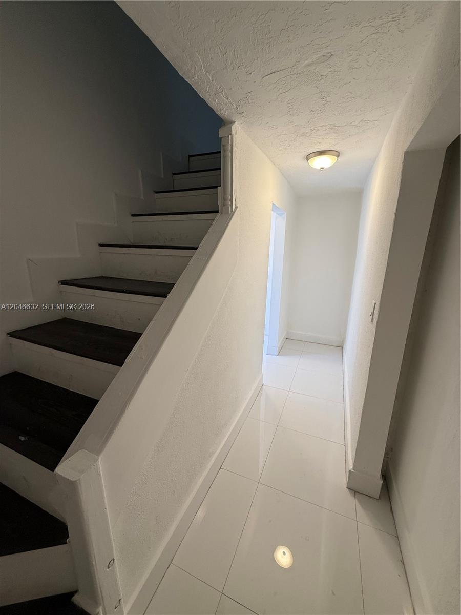 A staircase with dark wood treads and white risers sits beside a tiled hallway — 6716 NW 6th Ave # 2, Miami FL 33150, MIAMI, FL