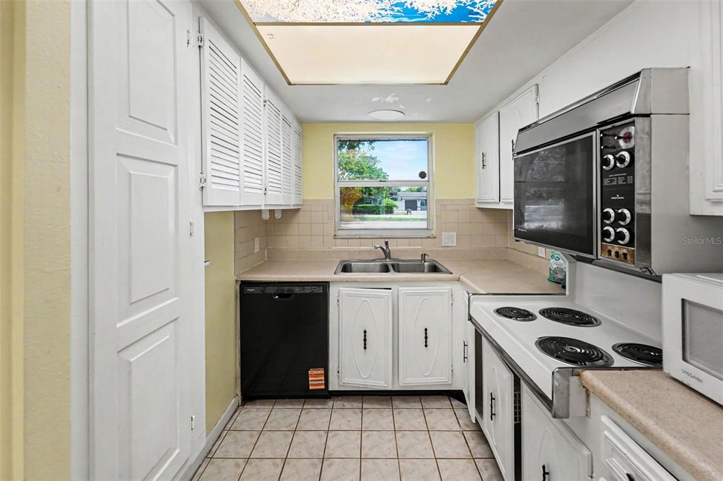 A galley kitchen features white louvered cabinets, a black dishwasher, and a window above the sink — 5870 38TH AVENUE N UNIT 43, ST PETERSBURG, FL