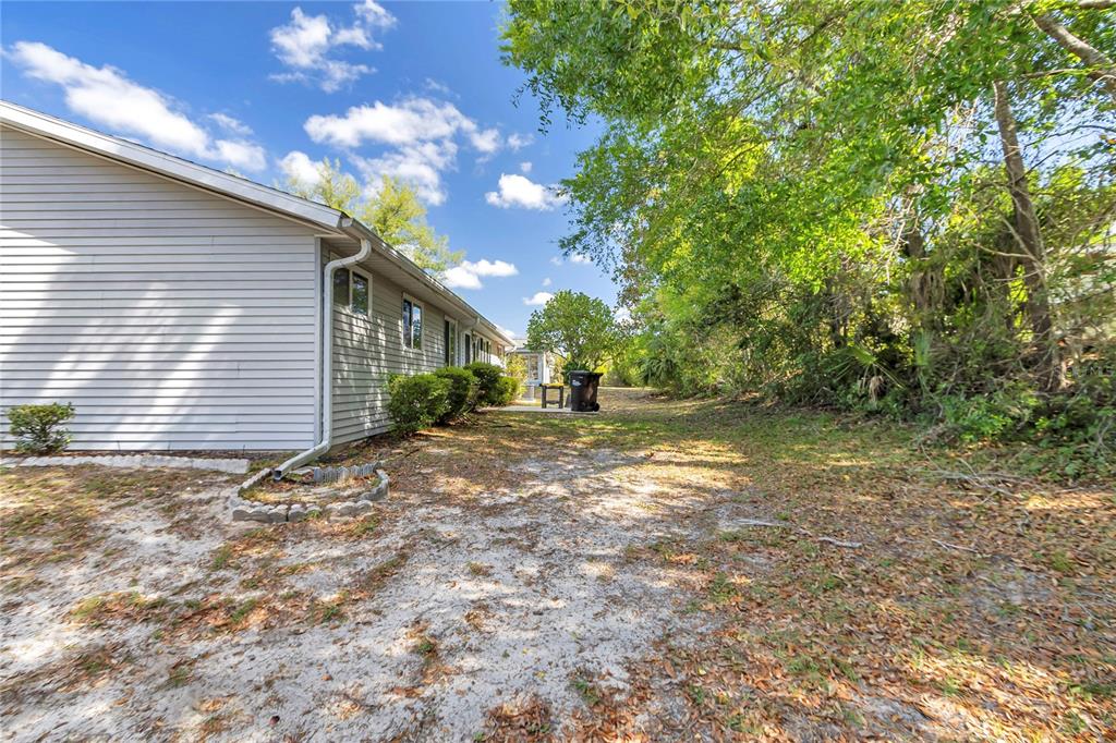 A side view of a house exterior with light siding, a sandy yard, and trees — 10891 SW 89TH AVENUE, OCALA, FL