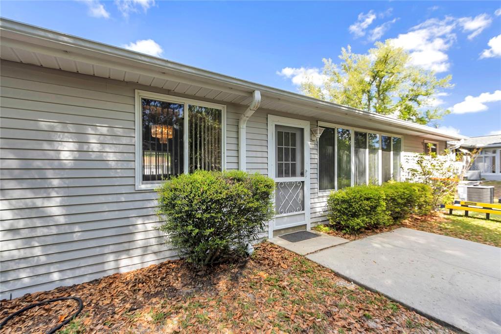 The exterior of a single-story house features light gray siding, a concrete patio, and landscaping — 10891 SW 89TH AVENUE, OCALA, FL
