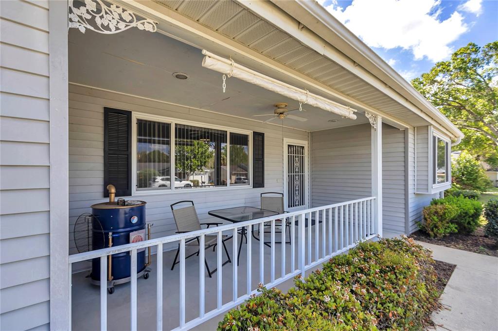 A covered porch features light gray siding, a white railing, outdoor furniture, and a blue barrel grill — 10891 SW 89TH AVENUE, OCALA, FL
