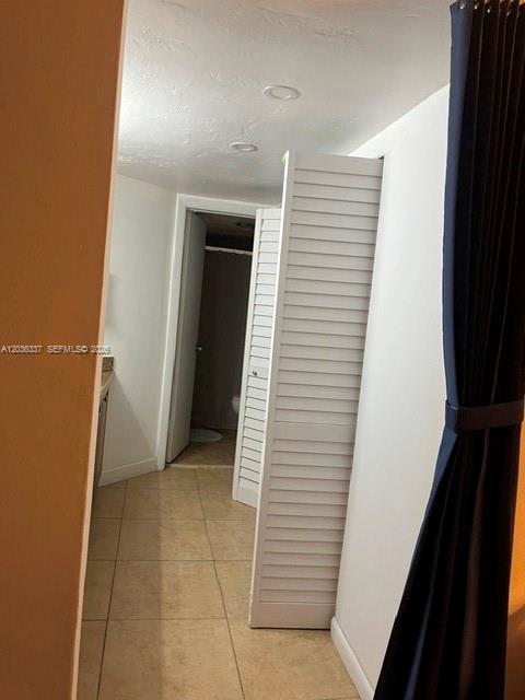 A hallway with beige tile flooring leads to a bathroom behind white louvered closet doors — 7410 SW 82nd St # K206, Miami FL 33143, MIAMI, FL