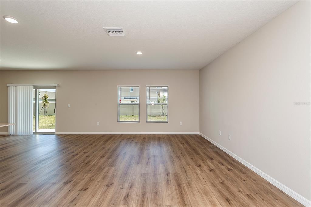An empty living room with wood-look flooring, two windows, and a sliding glass door — 2127 LAWSON WAY, ZEPHYRHILLS, FL