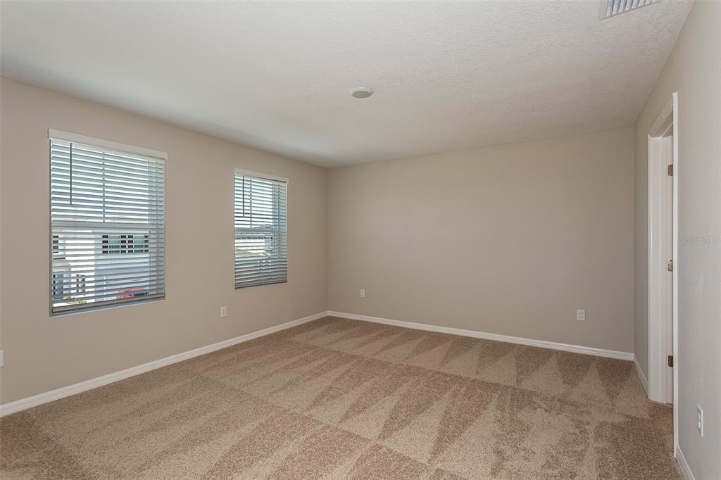 A carpeted bedroom with beige walls, two windows with blinds, and a doorway — 2127 LAWSON WAY, ZEPHYRHILLS, FL