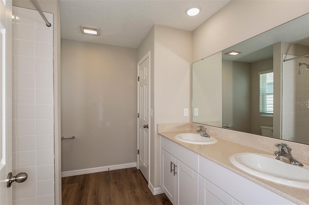 A bathroom features a double vanity with white cabinets, a large mirror, and wood-look flooring — 2127 LAWSON WAY, ZEPHYRHILLS, FL