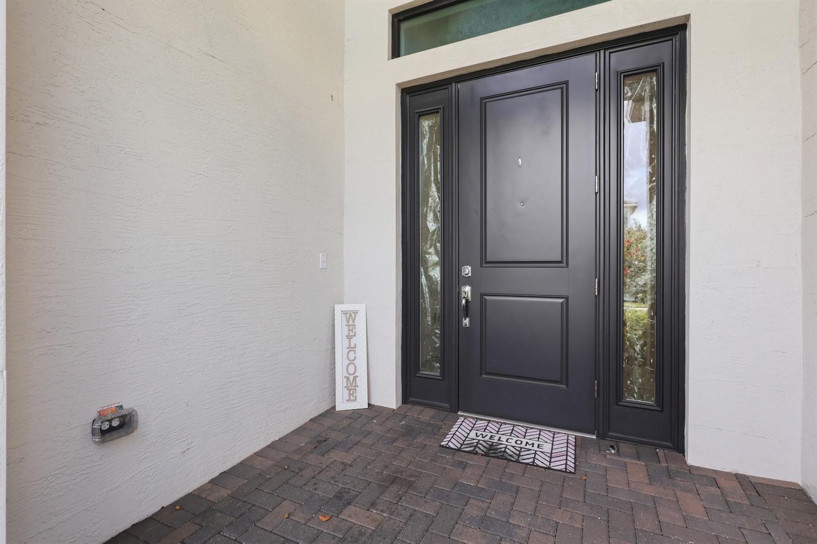 A dark front door with sidelights and a transom window sits on a brick porch — 5395 Saint Vincent Lane, FL 33470, FL