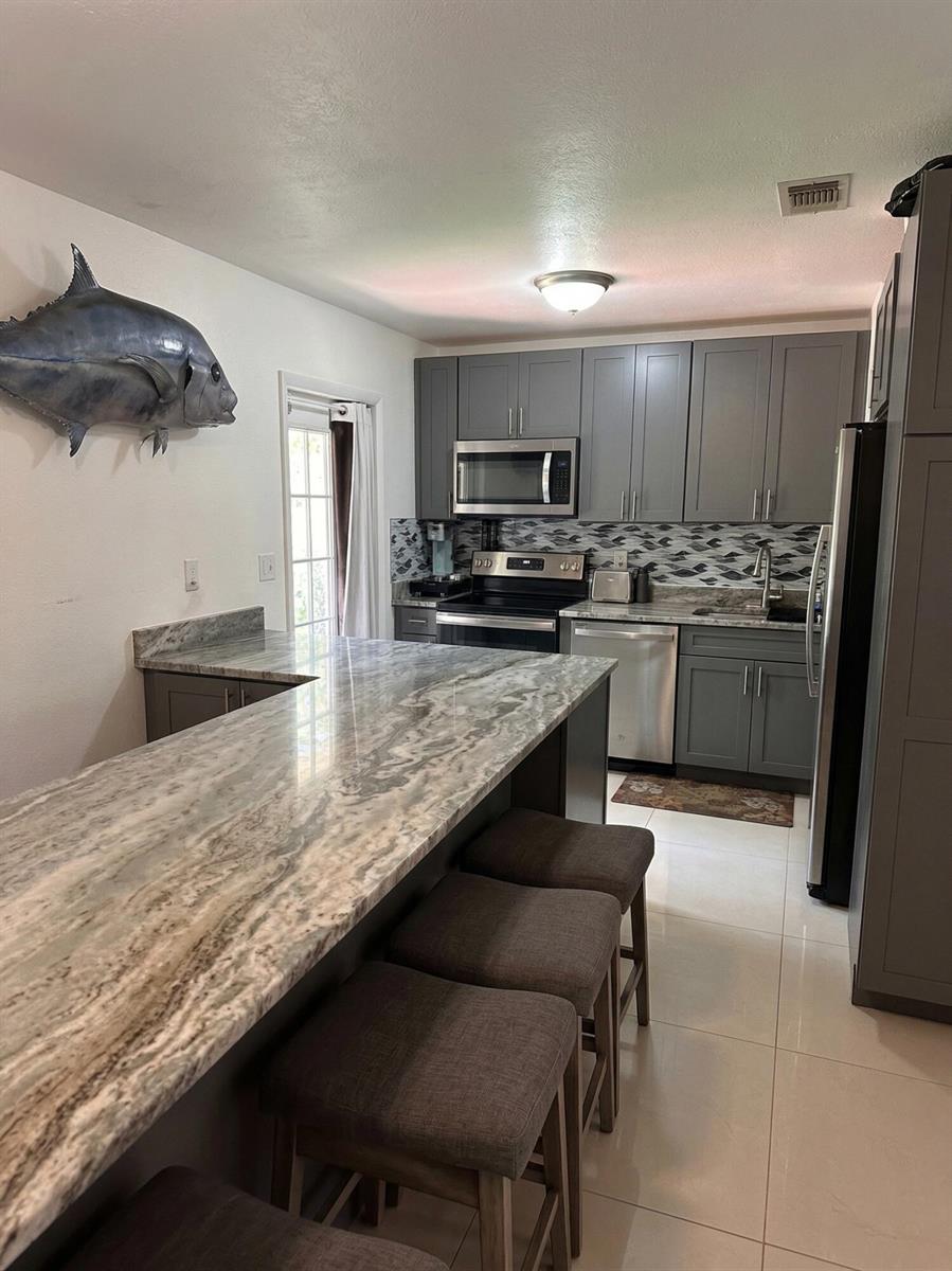 A kitchen features gray cabinets, a marble-topped island with three stools, and tile flooring — 1230 NE 26th Terrace, Pompano Beach FL 33062, POMPANO BEACH, FL