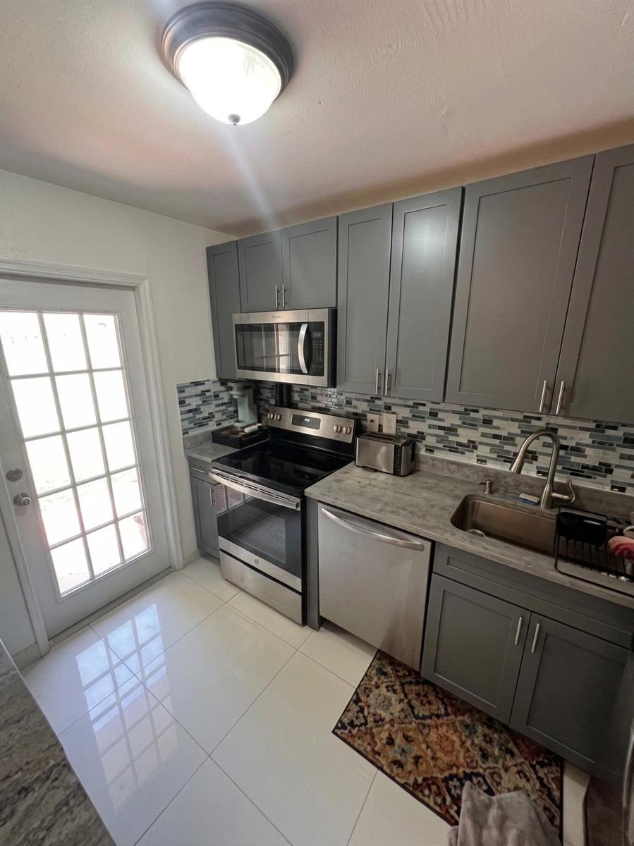 A kitchen features gray cabinets, a marble-patterned countertop, a breakfast bar, and stainless appliances — 1230 NE 26th Terrace, Pompano Beach FL 33062, POMPANO BEACH, FL