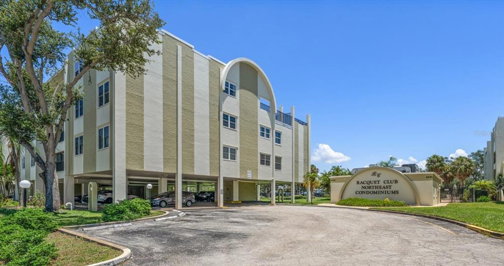 A multi-story condominium building features a covered parking area and a prominent entrance sign — 4681 1ST STREET NE UNIT 308, ST PETERSBURG, FL