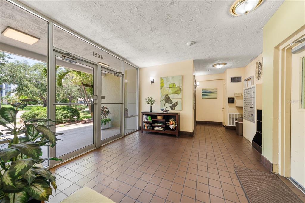 A tiled apartment building lobby features a glass entrance, a bookshelf, and wall-mounted mailboxes — 4681 1ST STREET NE UNIT 308, ST PETERSBURG, FL