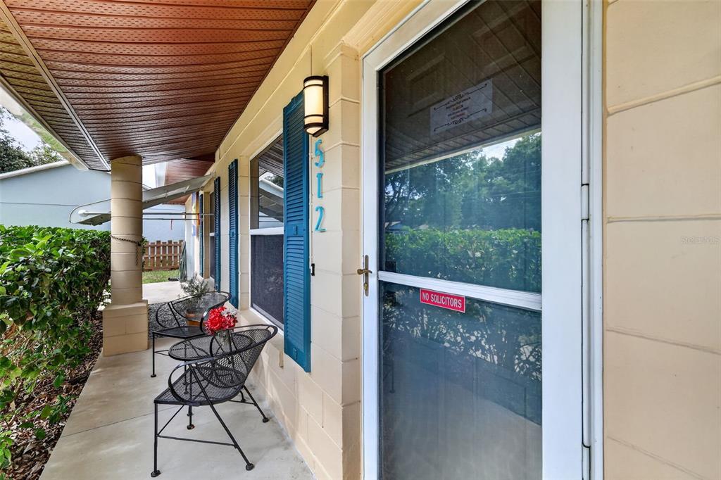 A covered front porch features a white door, blue shutters, and two metal chairs — 512 HIGHLAND DRIVE, EUSTIS, FL