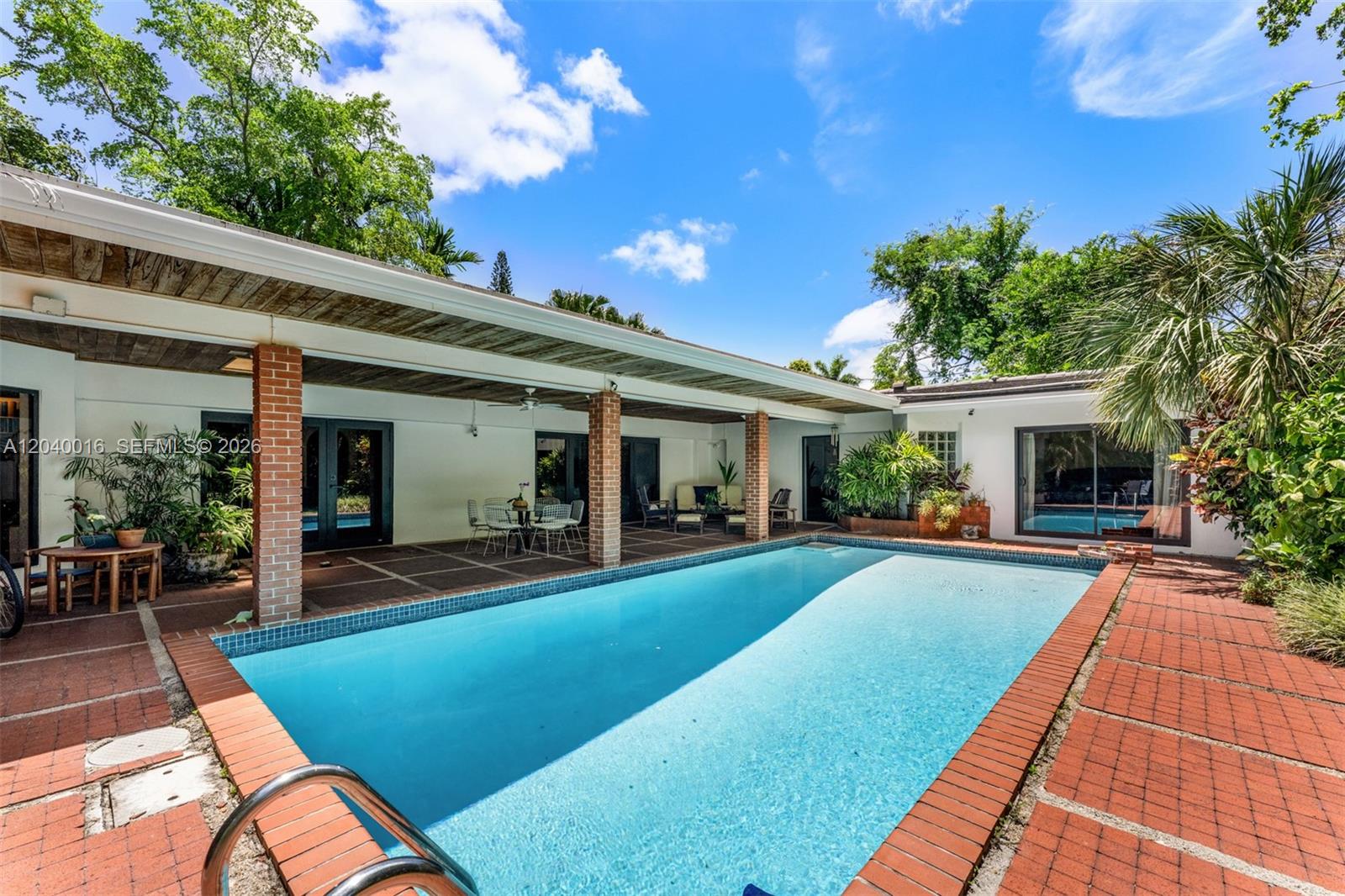 A rectangular swimming pool sits on a red brick patio beside a covered outdoor terrace — 11100 SW 67th Ave, Pinecrest FL 33156, PINECREST, FL