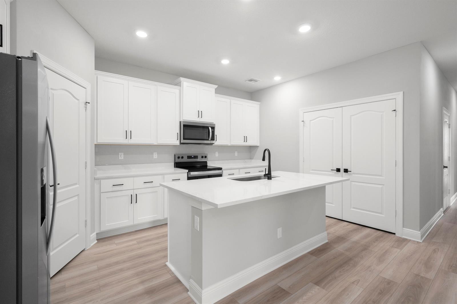 A modern kitchen features white cabinets, quartz countertops, a center island, and light wood flooring — 1611 Gaiety Way, Fort Pierce FL 34947, FORT PIERCE, FL