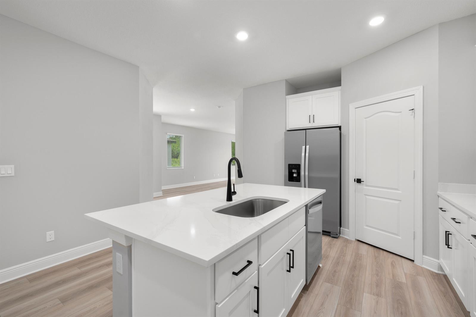 A kitchen island with a sink and white cabinets sits before a stainless steel refrigerator — 1611 Gaiety Way, Fort Pierce FL 34947, FORT PIERCE, FL