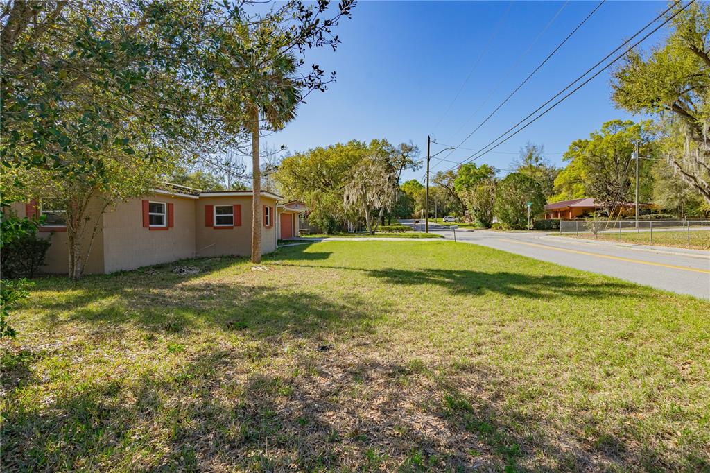 A view of a tan house exterior with red shutters next to a grassy yard — 805 S STONE STREET, DELAND, FL