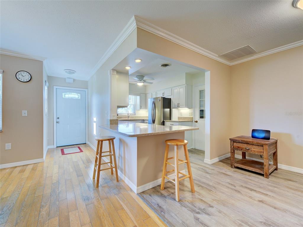 A kitchen with a granite breakfast bar and two wooden stools opens to a living area — 836 STEWART STREET, ENGLEWOOD, FL