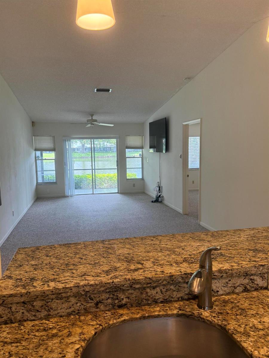 A kitchen counter with a granite top overlooks a living room with carpeted flooring — 18528 Hidden Way, Boca Raton FL 33496, BOCA RATON, FL