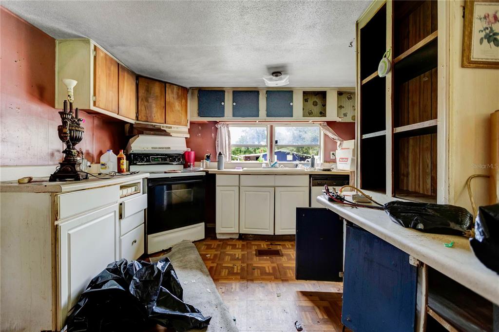 A kitchen with wood-paneled walls, white cabinets, a black stove, and worn parquet flooring — 2614 KYLE STREET, LAKELAND, FL