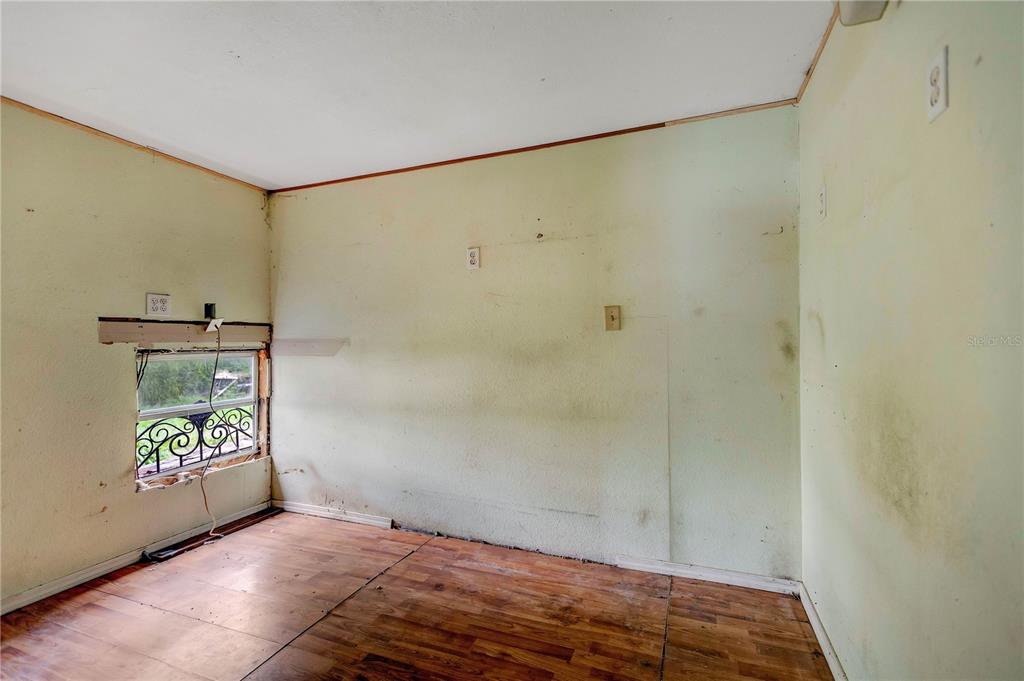 An empty room features wood-look flooring, light green walls, and an unfinished window area — 2614 KYLE STREET, LAKELAND, FL