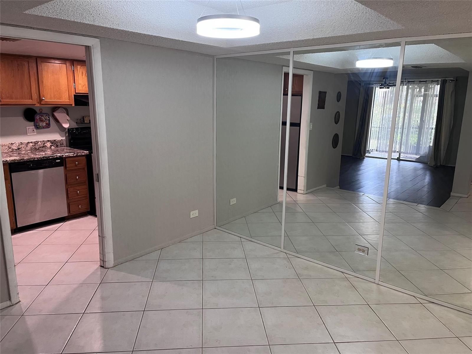 A room with tiled floors and mirrored walls leads to a kitchen with wooden cabinets — 3670 N Inverrary Drive # 1F, Lauderhill FL 33319, LAUDERHILL, FL